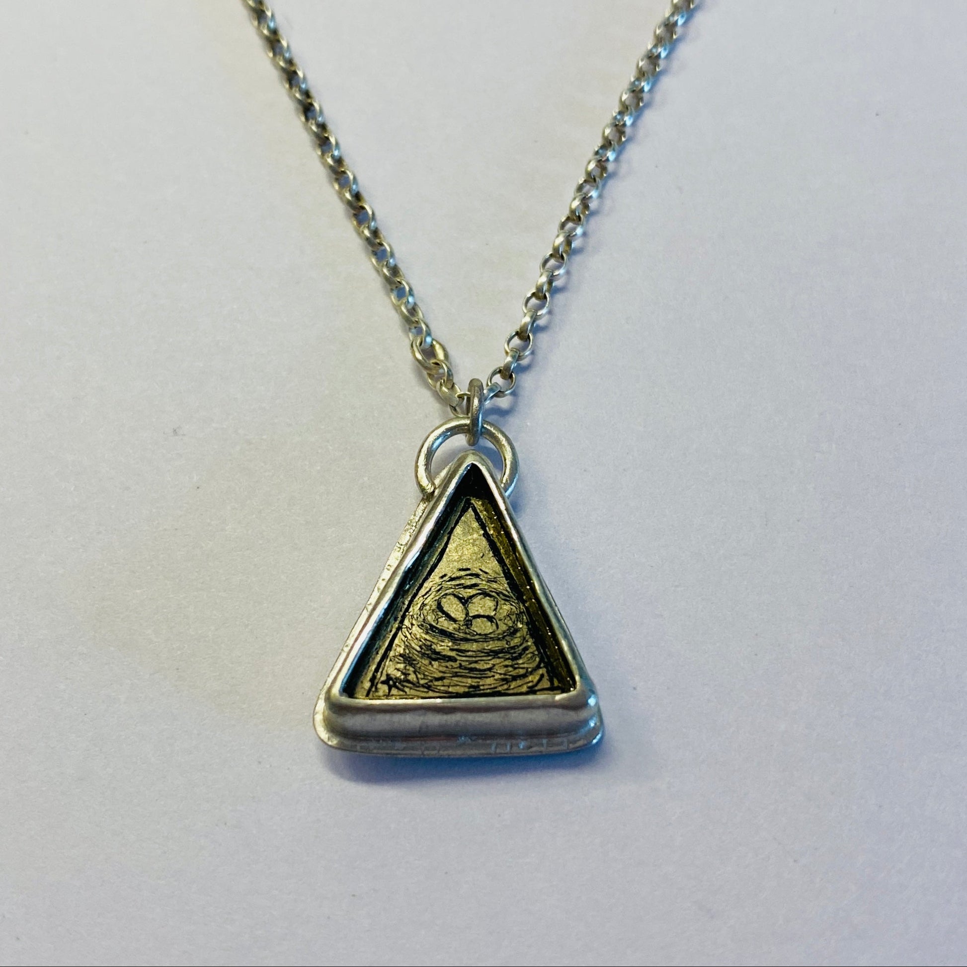 Necklace with a triangular pendant depicting a birds nest with eggs.