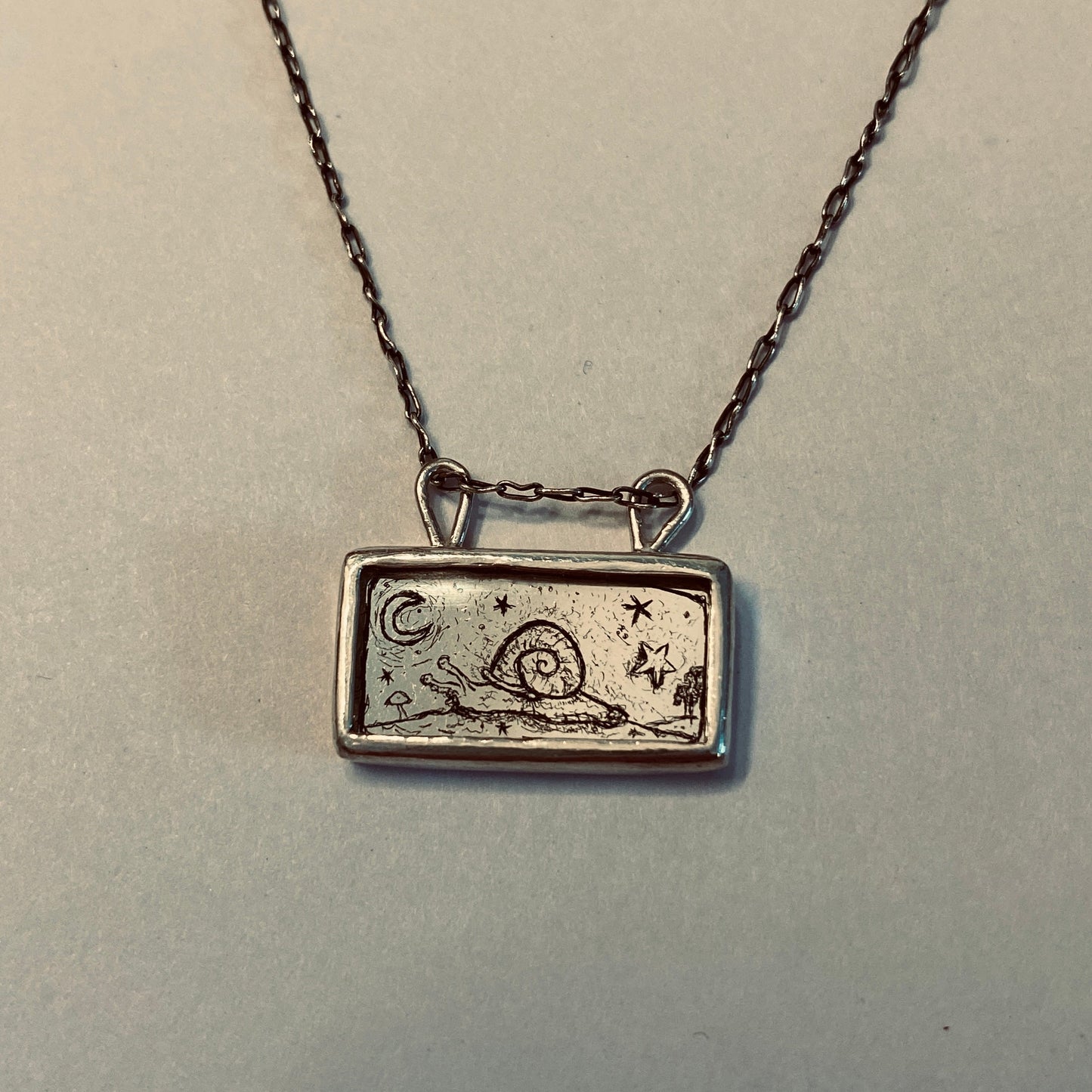 Silver necklace with a rectangular pendant featuring a snail design etched into gold leaf