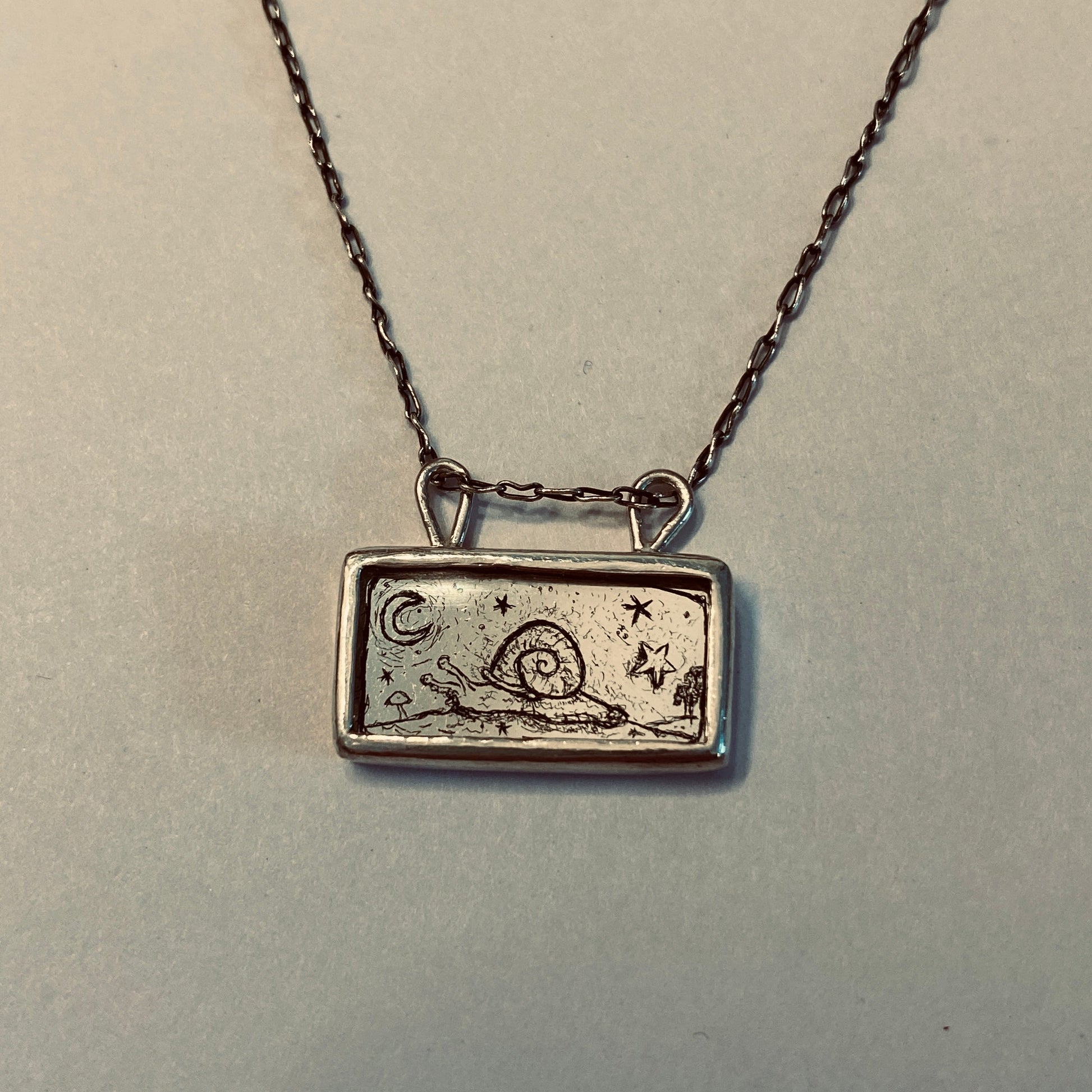 Silver necklace with a rectangular pendant featuring a snail design etched into gold leaf