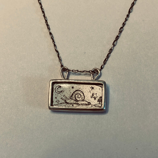 Silver necklace with a rectangular pendant featuring a snail design etched into gold leaf